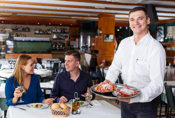 Fototapeta na wymiar Waiter in white shirt showing tray of lobsters serving for couple visitors