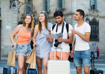 portrait of four smiling adult travelers holding map in hands and looking for their way in town