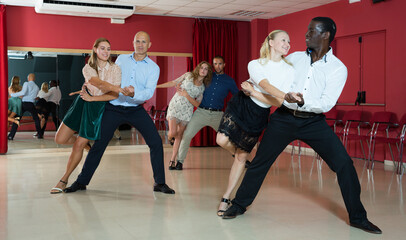 Portrait of positive adult pairs enjoying tango in modern dance hall together