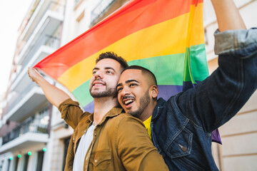 Gay couple embracing and showing their love with rainbow flag.