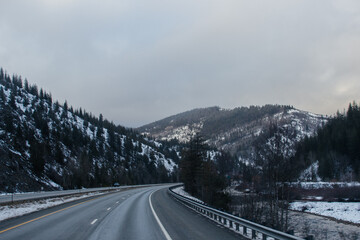 Winter Highway, on which cars and trucks travel, among the mountains covered with snow. Winter road landscape at sunset with beautiful sky of blue and pink shades. Hwy 90, Idaho, USA. 2-8-2020