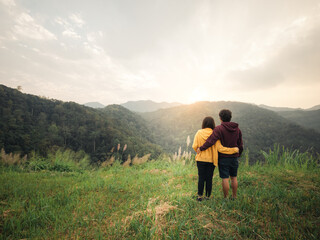 Fototapeta na wymiar couple making heart shape with hands and enjoy the sunset view on mountain peak at Mae Wong national park Thailand.