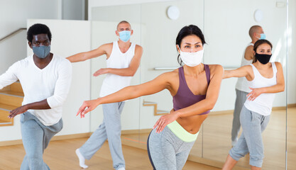 Multiethnic group of adult people wearing face masks for viral protection practicing active dancing in class