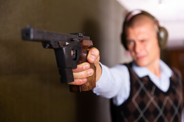Focused shooter practicing sport handgun shooting at firing range. Selective focus on male hand squeezing pistol grip and pressing trigger.