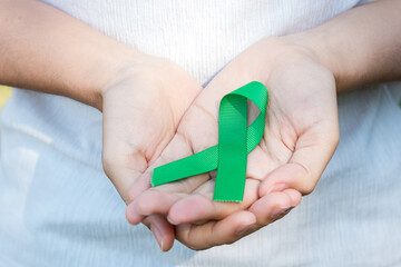 Woman holding green Ribbon for supporting people living and illness. Liver, Gallbladders bile duct, kidney Cancer and Lymphoma Awareness month concept