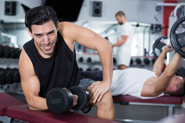 Fototapeta na wymiar Portrait of handsome athletic man exercising with dumbbells in gym