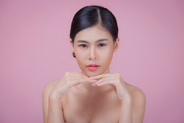 Youthful smiling Asian woman with hand touching face isolated on pink background for beauty and skin care concepts