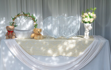Heart box and teddy bear beside the basket on the table covered with white cloth.