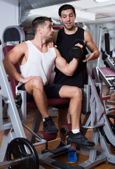 Fototapeta na wymiar Athletic man helping friend to performing exercises on fitness machine in gym