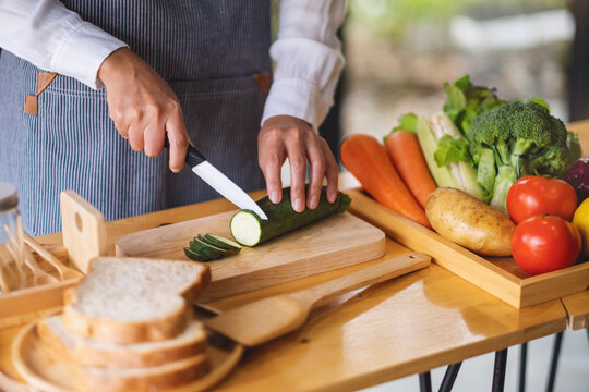 Closeup image of a female chef cutting and chopping vegetables by knife on wooden board in kitchen