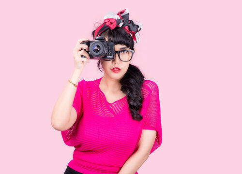 Like taking pictures. Closeup woman Holding camera pretty smiling pinup girl button shirt thinking about love career money looking hopeful to side, retro vintage 50's hairstyle isolated on color pink 