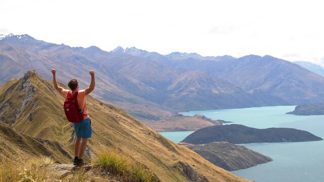 Travel hiker with view of amazing mountain lake nature landscape on New Zealand on famous Wanaka hike to Roys Peak. Happy hiking man jumping having fun in nature on New Zealand. 59.94 FPS SLOW MOTION.