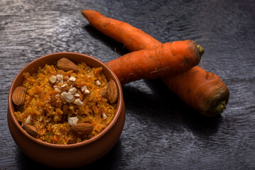 Gajar ka halwa is a carrot based sweet dessert from India. Garnished with Cashew and almond nuts and Served in a bowl over black background.