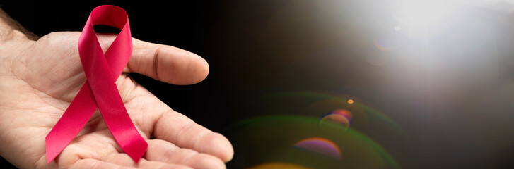 Red awareness ribbon in the hands of a man on a dark background with a place for text for the...
