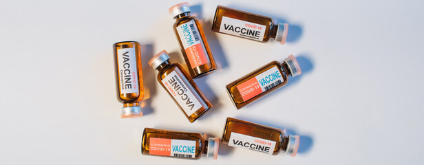 Vials of different coronavirus vaccine lie randomly on white background, close-up. Covid-19 banner with copy space. Completion of development of antiviral drug, mass vaccination of population.