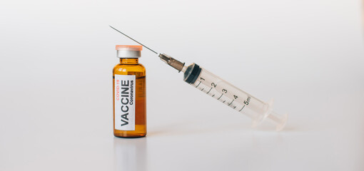 Coronavirus covid-19 vaccine vial with label, syringe for injection on white background with copy space. Medical needle lies on the bottle with drug. Vaccination, immunization concept.