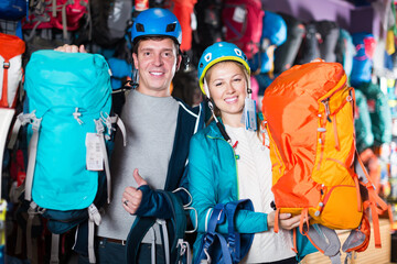 Fototapeta na wymiar Young pair in sports shop shows reliable backpacks for hiking.