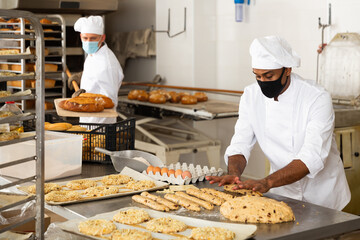 Portrait of male baker in face mask working with dough and forming baguettes