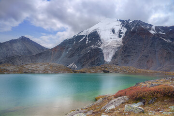 Mountain landscape. High mountain and green lake. Selective focus on the snowy mountain peak.