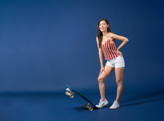 Fototapeta na wymiar Happy young Asian woman standing on surfskate or skateboard on blue color background, exercise and sport, trendy and extream sports concept