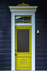 Yellow door with white wooden frame on dark blue wall, french style, in New Orleans (LA) USA