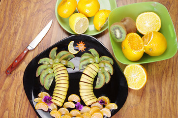 Fruit carving. Fruit dessert made from sliced bananas, kiwi, tangerines laid out on a plate in the shape of tropical palms. 