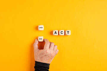 The word act on wooden blocks with a male hand choosing the now option. Taking action