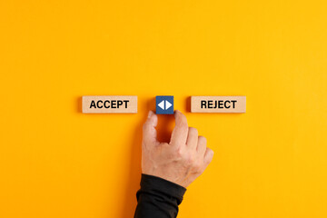 Male hand holds a wooden cube with arrow icon between the options of accept or reject.