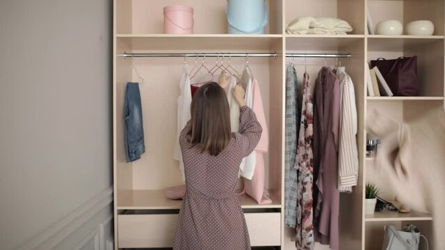 Different clothes hang in wardrobe on hangers, concept of organization and storage of things. Young woman throws things out of the closet trying to find something to wear. Female's problem.