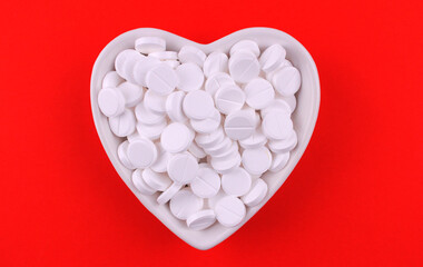 White round pills in heart shaped cup on red background