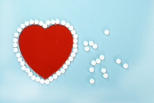 On a blue background lies a red heart whose outline is made of white round tablets. Concept photo