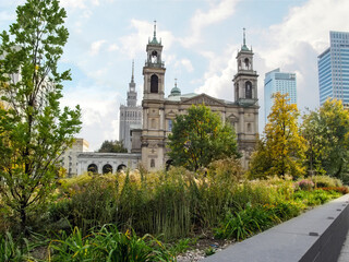Naklejka premium Flowerbed with green autumn plants in the background of All Saints Church and PKiN in Warsaw, Poland. Cityscape of the Polish capital with historical tourist attractions, background with copy space