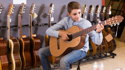 happy teenage boy choosing best acoustic guitar in musical shop.