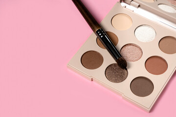  Daily eyeshadow palette in brown tones on a pink background top view with copy space. makeup brush, decorative cosmetics for the face. Flat lay female accessories. Nobody - obrazy, fototapety, plakaty