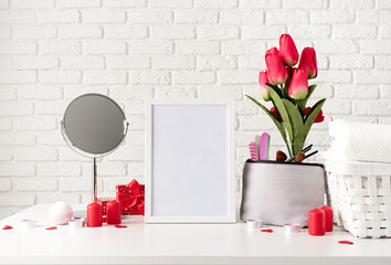 cosmetic and spa accessories with gift box, flowers and candles on dressing table front view on white brick wall background with blank frame for mock up