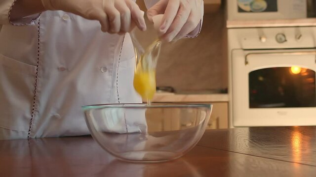Cropped image of a cute pastry chef girl breaking an egg into a bowl and stirring with a culinary broom. Slow motion