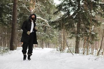 Outdoor portrait of handsome man in coat and scurf. Bearded man in the winter woods.