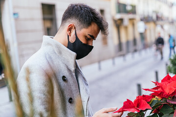 Shallow focus of a young male with a facemask choosing flowers from a shop outdoors