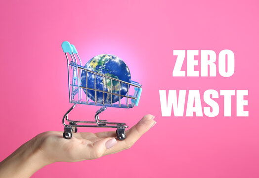 Female hand with small planet Earth in shopping cart on color background. Zero waste concept