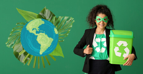 Woman dressed as superhero with trash bin near drawing of planet on color background. Earth Day...