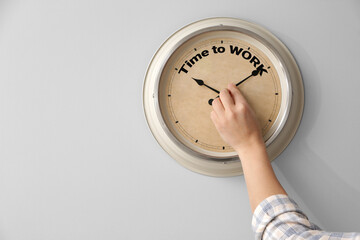 Man touching arrows of clock with text TIME TO WORK on light wall