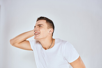 Emotional man in a white t-shirt holds his hand on his face light background
