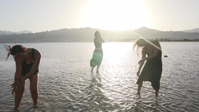 group of wet attractive females dancing ecstatic in sea at sunset slow motion