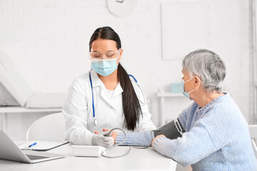 Fototapeta na wymiar Doctor measuring blood pressure of senior woman in clinic