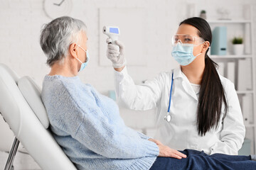 Doctor measuring temperature of senior woman in clinic