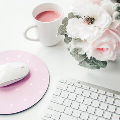 white workspace with light pink note book and white flower with coffee on white table.