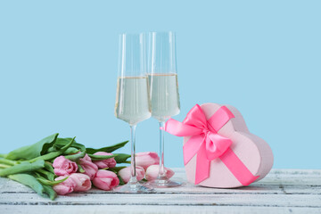 Glasses of champagne, gift for Valentine's Day and flowers on table