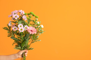 Hand with bouquet of beautiful flowers on color background