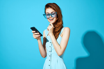 woman in blue dress with glasses holding a phone technology call blue background