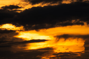 Fototapeta na wymiar Golden sunset sky with dark clouds. Beauty in nature. Beautiful sunset sky abstract background. Orange and yellow sky with black clouds at dusk. Sky at dusk. Peaceful and tranquil concept.